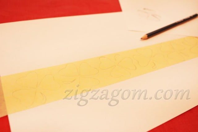 Наклеить полоску малярного скотча на лист бумаги и с помощью подготовленного трафарета нарисовать на ней трилистники